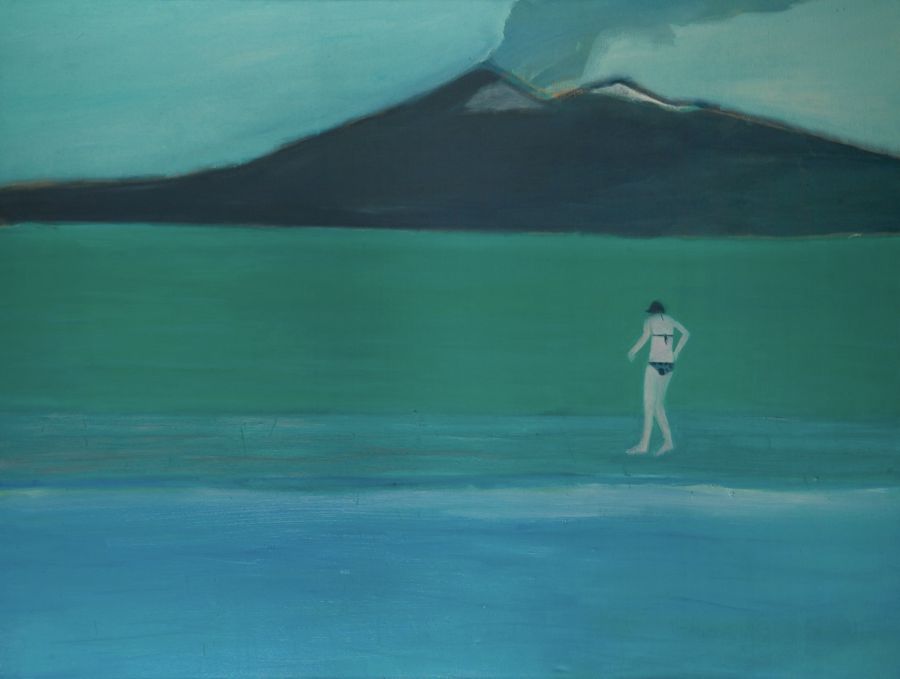 A figure on the seashore with a volcano behind.